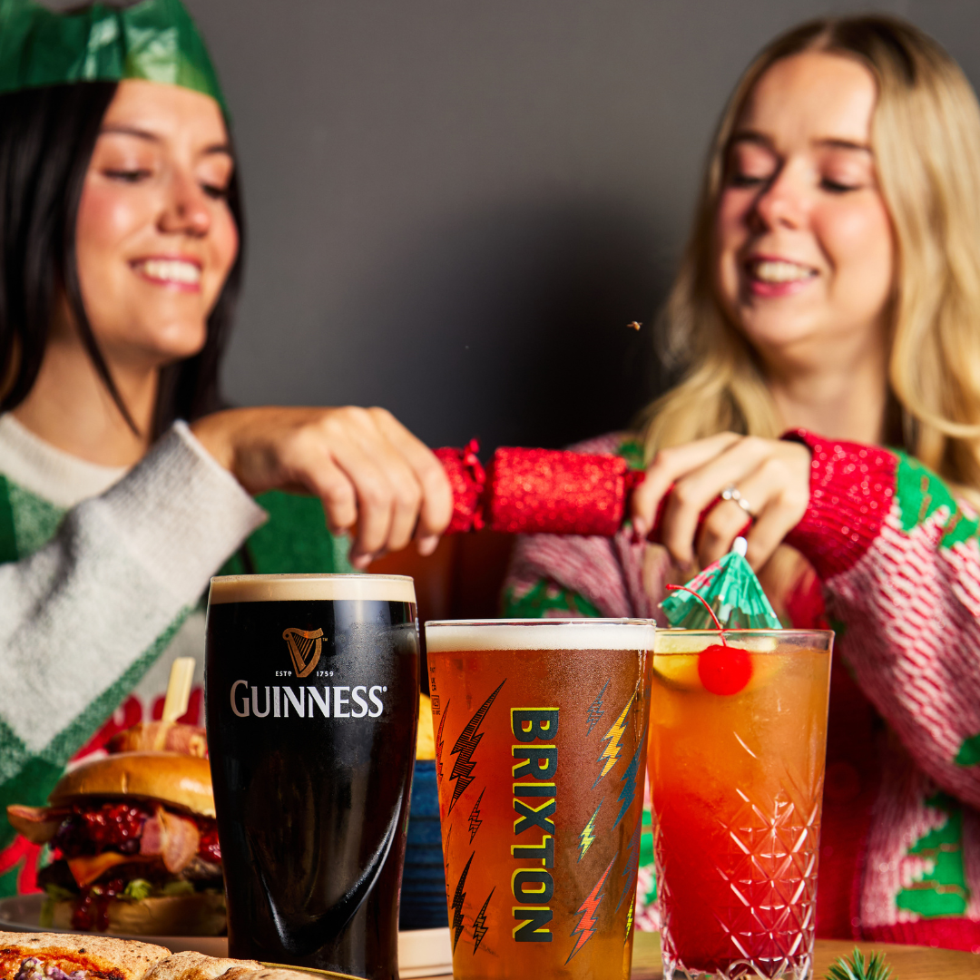 2 people pulling a cracker with drinks on table